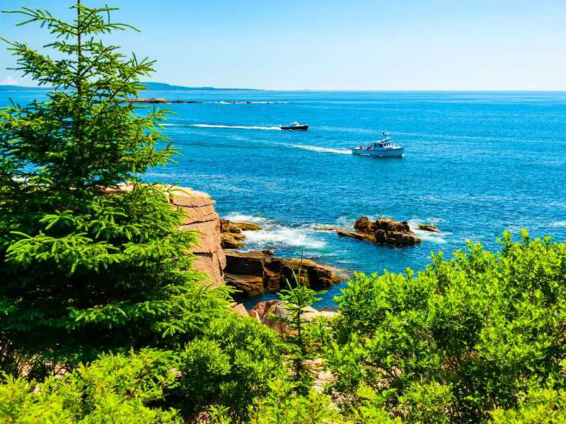 Two small boats in the middle of the ocean in front of rocky cliffs and trees in Acadia National Park