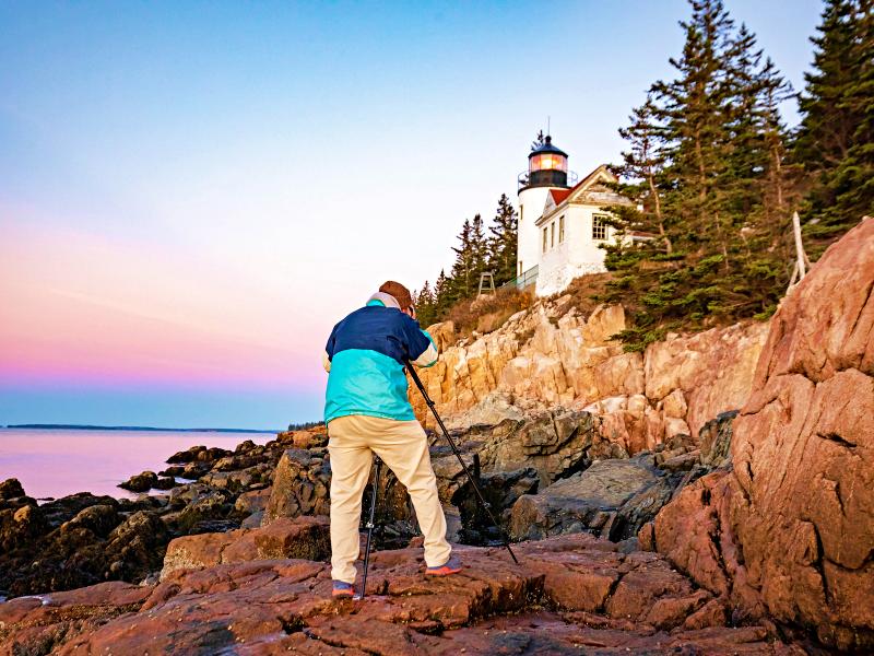 Man taking pictures of the lighthouse in the rocky place beside the ocean in Acadia National Park