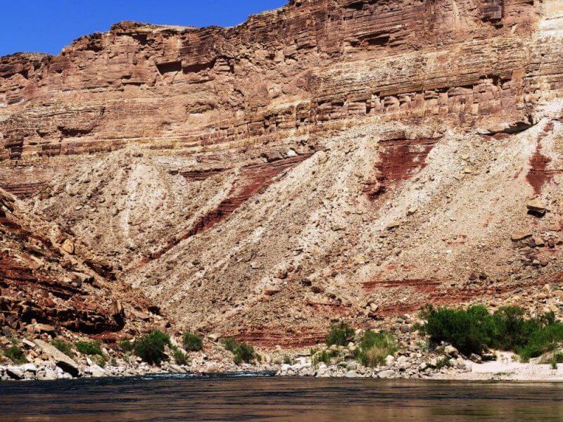 tiny boat surrounded by towering cliffs of grand canyon on river rafting trip through grand canyon