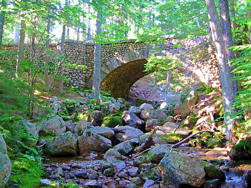 Stone bridge surrounded by trees and below are rocks with flowing water, one of the carriage roads in Acadia National Park