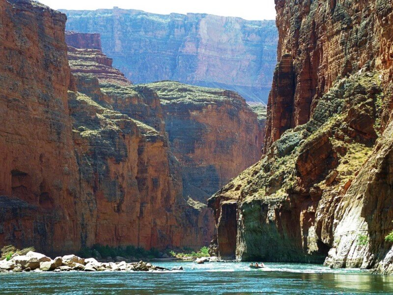 rafts and wooden boats going through rapids inside large canyon on river trip through grand canyon