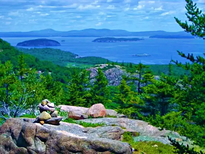 Aerial view of an ocean, islands, and mountains filled with trees from the huge stone in Beehive Trail in Acadia National Park.