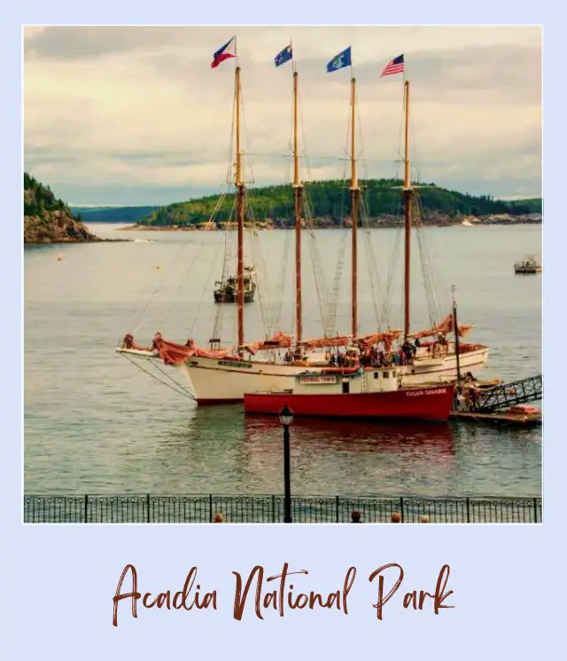 A mountain in the ocean coast and a docked boat with four flags of different countries on it in Sailing Acadia National Park