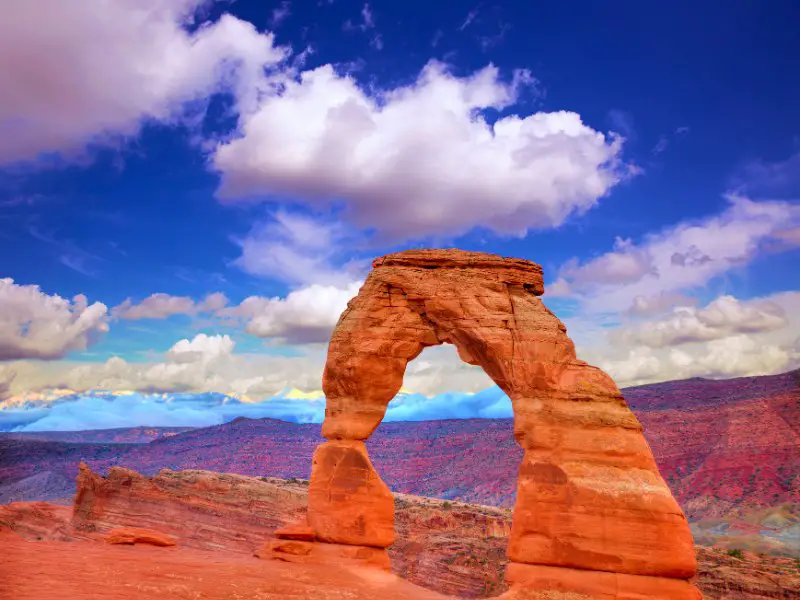 A huge rock arch and behind are rock mountains under the blue sky in Arches National Park
