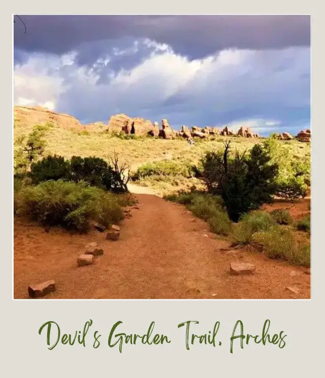 View of upward Trail surrounded bt bushes and above are huge rock formations in Devils Garden in Arches National Park.