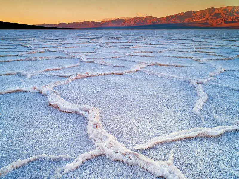 Salt forming on the ground of Badwater Basin in Death Valley National Park, and on the other side are mountain ranges.