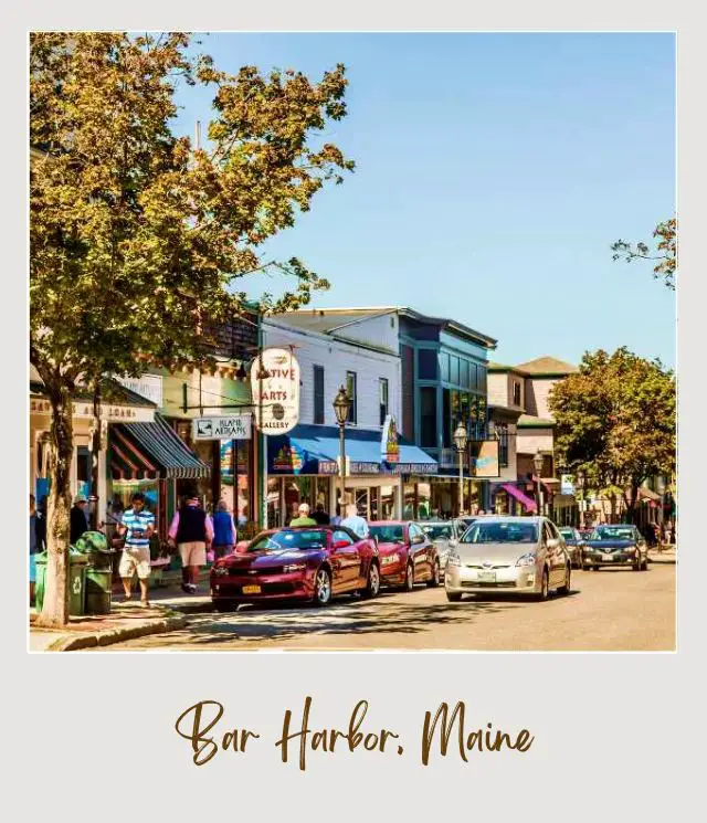 Parked cars and moving cars in the middle of the road and beside buildings, people are walking surrounded by trees in Bar Harbor near Acadia National Park.