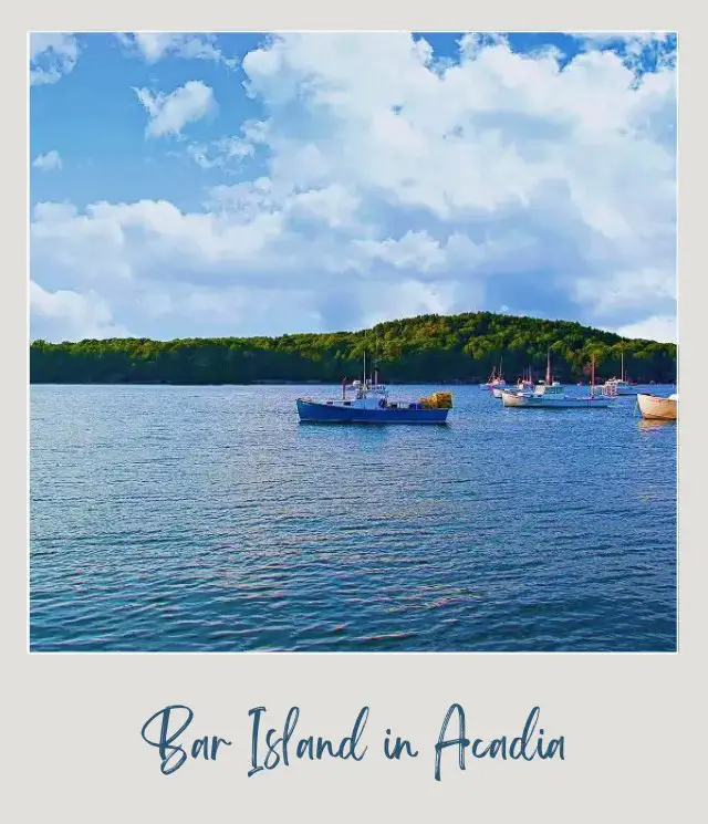 Small boats are in the middle of the blue oceans, and behind is an island surrounded by trees in Acadia National Park