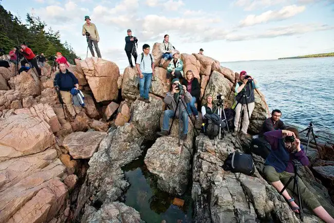 lots of people on rocks with cameras on tripods all waiting for sunset to photograph Bass Harbor Head Lighthouse in Acadia National Park