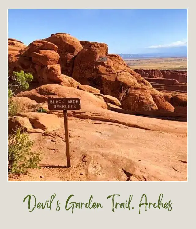 Wooden signage and behind are huge rock formations on Devils Garden Trail in Arches National Park.