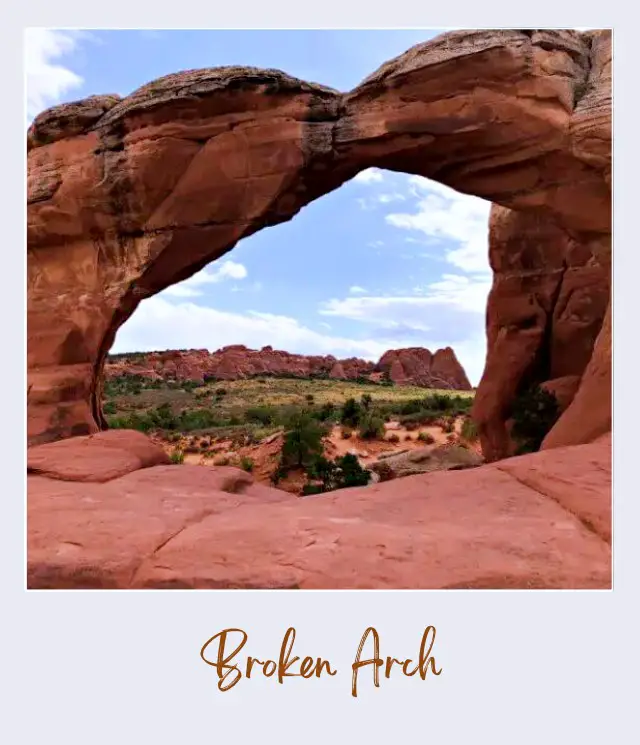 View of huge rock formations and mountains at the distance from the huge rock-forming tunnel at Broken Arch in Arches National Park.