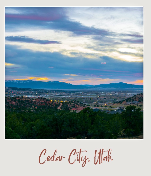 Small trees are in the middle of hills, and below the mountain are building in Cedar City, Utah, on the opposite side