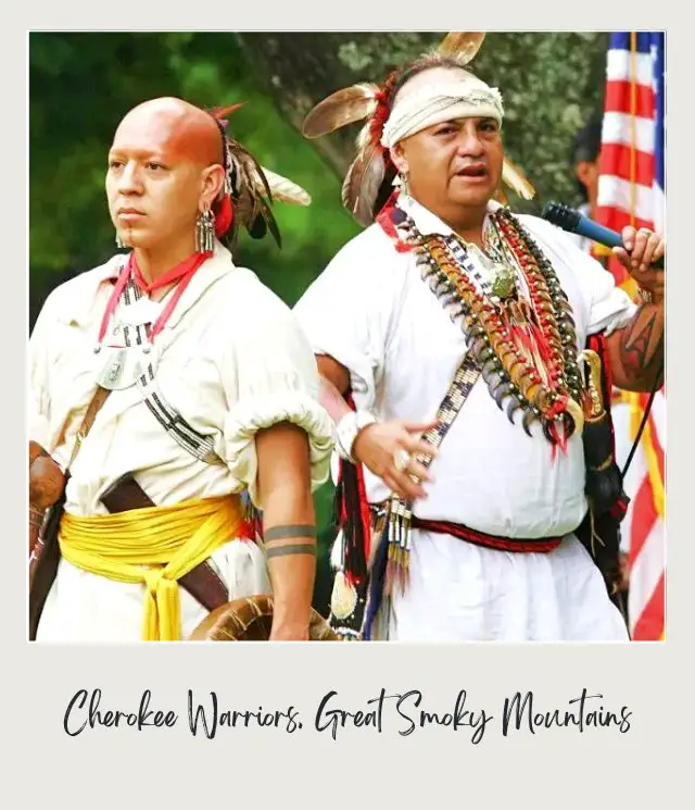 Two men wearing traditional attire, and behind is the flag of the United States of America.