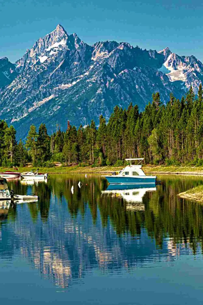 Small ships on the ocean and besides are trees and behind is a snow-capped mountain