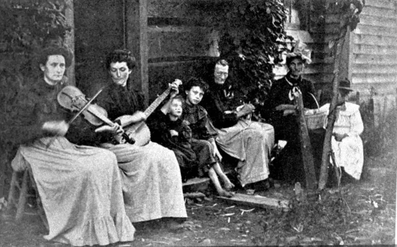 Black and white photo of a family consisting of seven people, two of them holding music instruments.