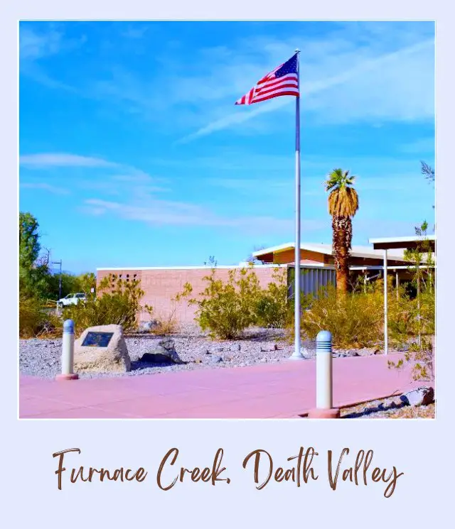 The flag of the USA hangs on the pole in front of a building surrounded by busses and palm trees in Furnace Creek in Death Valley National Park.