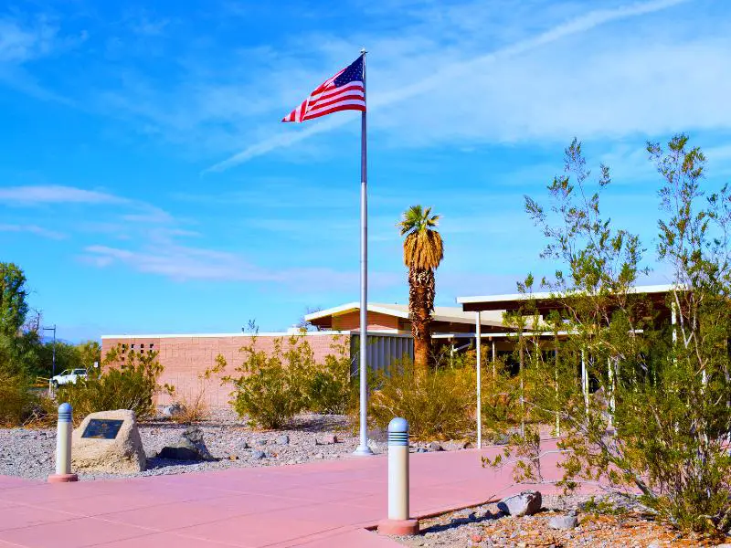 The flag of the USA hangs on the pole in front of a building surrounded by busses and palm trees in Furnace Creek in Death Valley National Park.