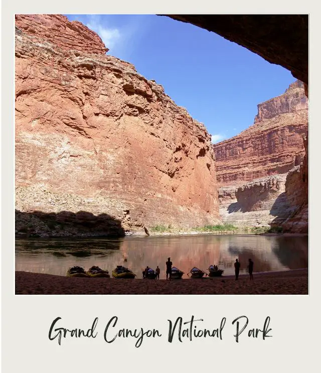 boats and rafts drawn up on beach inside large cavern looking out at canyon walls and river on river trip through grand canyon