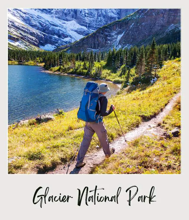 A person carrying a backpack hiking on a trail surrounded by mountains in Glacier National Park.