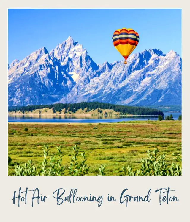 A colorful hot air balloon is in the air, and below is a lake surrounded by mountains and grass fields in Grand Teton National Park.