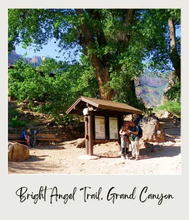 People resting under the trees with the signage below the mountains in Bright Angel Trail in Grand Canyon National Park.