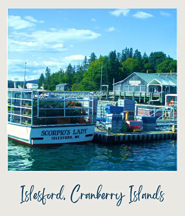 Small Cargo boats are in the water and behind is a house surrounded by trees under the blue sky on the Cranberry Islands, one of the things do near Acadia National Park