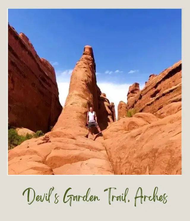 View of James standing on Devil's Garden Trail and behind are huge rock formations in Arches National Park.