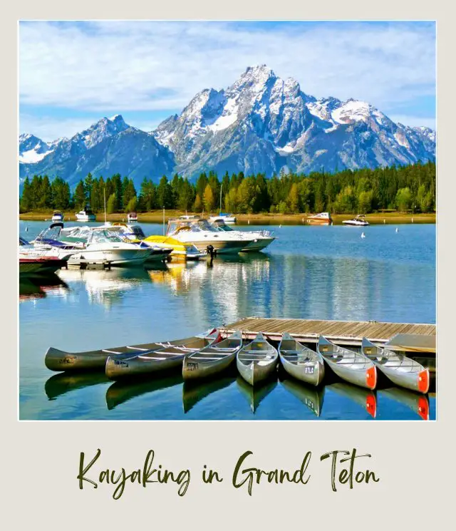 Small boats and kayaks beside the wooden bridge on the water, and behind are trees and snow-capped mountains in Grand Teton National Park.