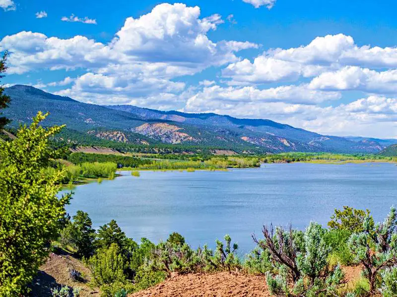 Lake surrounded by trees, and behind is the mountain under the cloudy blue sky near Cortez Airport