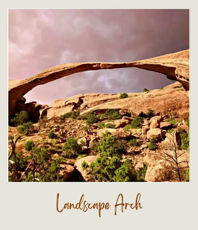 View of rock-forming arch surrounded by bushes and other rocks in Devils Garden in Arches National Park.