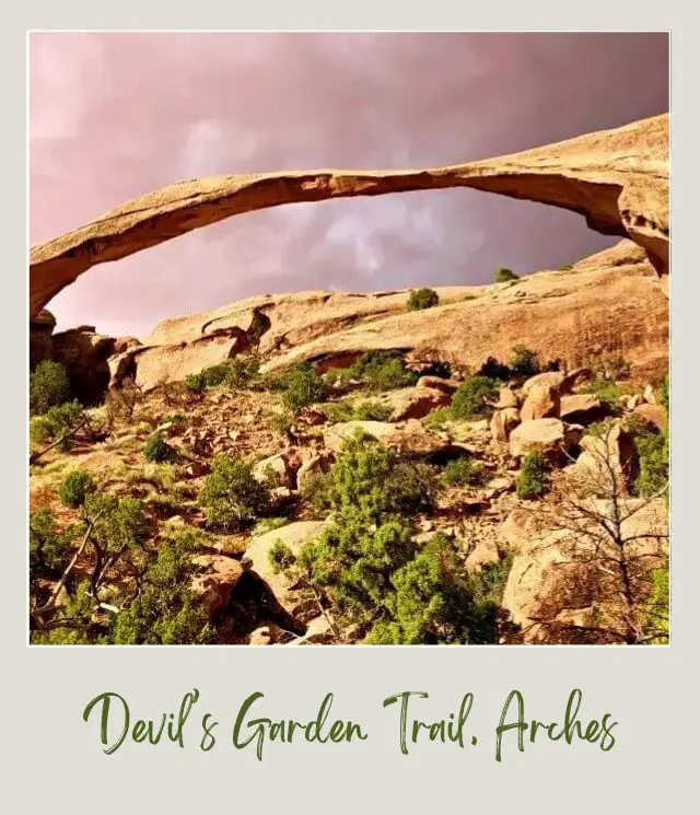 View of rock-forming arch surrounded by bushes and other rocks in Devils Garden in Arches National Park.