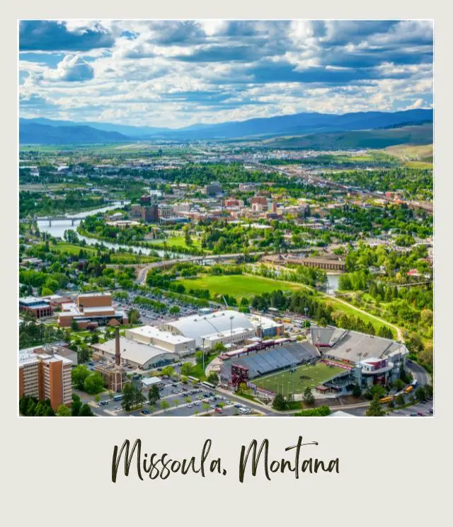 Aerial view of Missoula Montana, with buildings surrounded by trees, highways, cars and mountains.