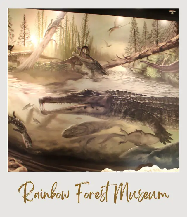 Museum mural depicting a prehistoric swamp scene with large crocodile-like reptiles in the water, fish swimming beneath them, flying reptiles in the sky, and a forest of tall trees in the background.