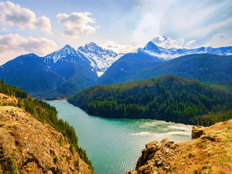 View of snow-capped mountains, trees, and a lake in North Cascades National Park.