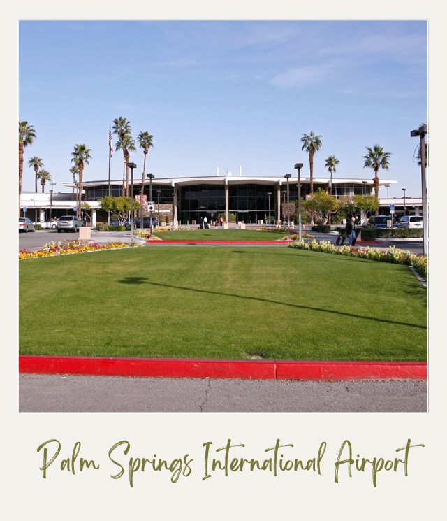 View of the airport building surrounded by palm trees and in front is a parking lot and lawn grass in Palm Springs International Airport in Joshua Tree National Park.