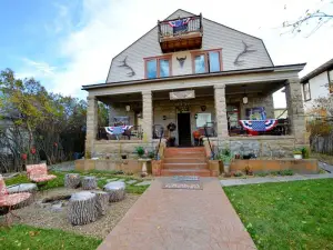 View of a two-story stone house with a wide front porch decorated with patriotic red, white, and blue banners in Park Hotel Yellowstone.