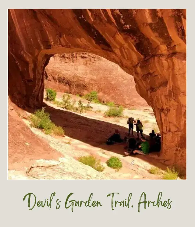 A group of people taking shelter under the huge rock on Devils Garden Trail in Arches National Park.