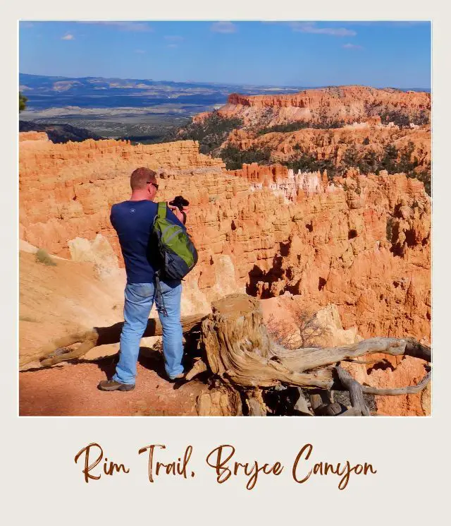 View of James holding a camera at Rim Trail facing the rock mountains and hoodoos in Bryce Canyon National Park.