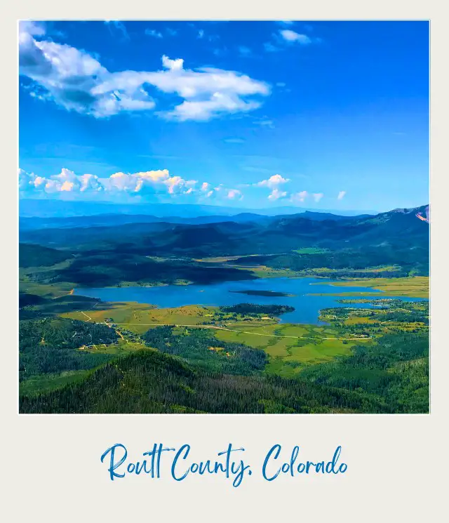 Aerial view of blue water lake surrounded by green trees and mountains in the middle of the day in North Routt Colorado near Yampa Valley Regional Airport.