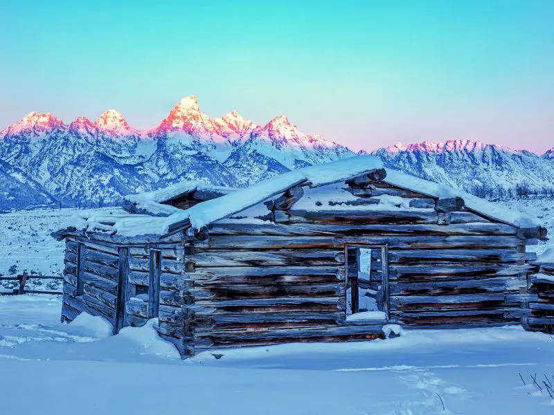 Wooden cabin covered with snow surrounded by snow-capped mountains