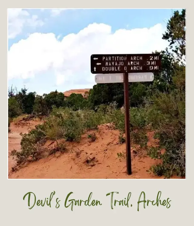 Trail surrounded by bushes and a wooden signage to Navajo Arch in Devils Garden in Arches National Park.