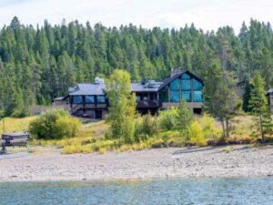 Large lakeside lodge with blue-tinted windows, rocky shoreline, and forest backdrop in Signal Mountain Lodge