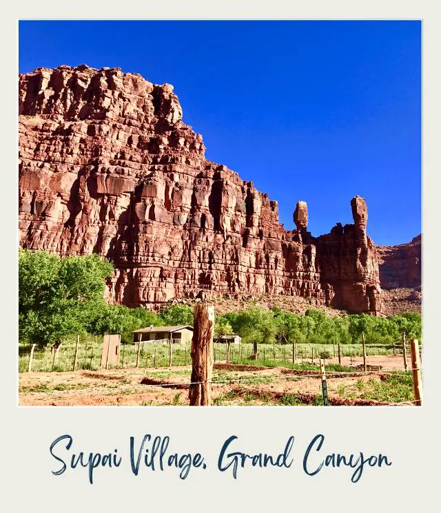 Huge rock formations and below are small wooden houses surrounded by trees in Supai village Grand Canyon National Park