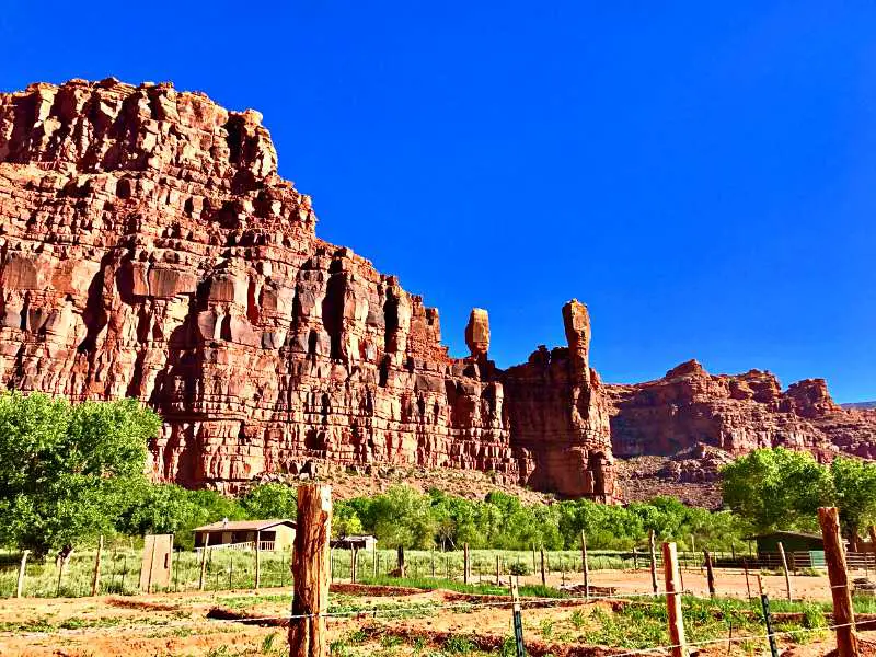 Huge rock formations and below are small wooden houses surrounded by trees in Supai village Grand Canyon National Park