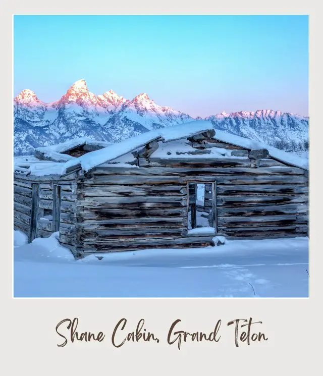 Wooden cabin covered with snow surrounded by snow-capped mountains