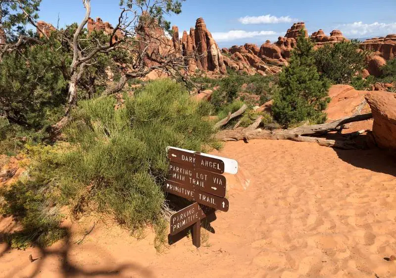 Trail signs with sandy path and rocks in background