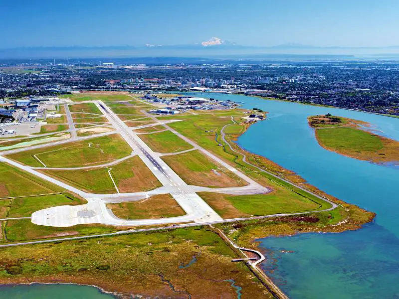 Vancouver International Airport in the middle of the day surrounded by blue water and grassland and on the opposite side is buildings in the city of Vancouver in British Columbia, Canada