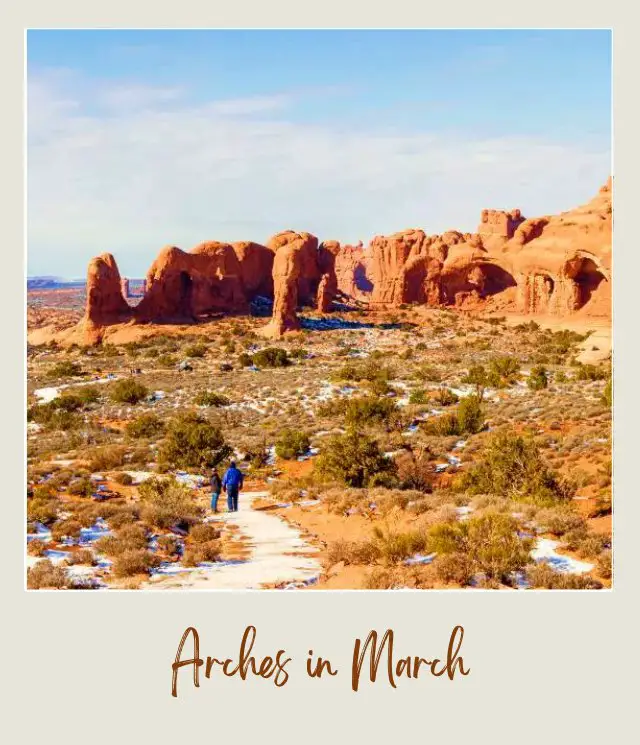 Two people surrounded by bushes covered with little snow and behind are huge rock formations in Arches National Park