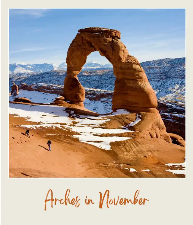 People walk around the huge rock arch and behind are rock mountains covered with snow in Arches National Park.