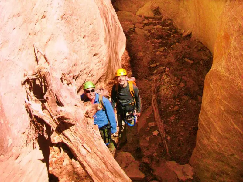 Two people wearing hats and gear in between huge rocks in Bryce Canyon